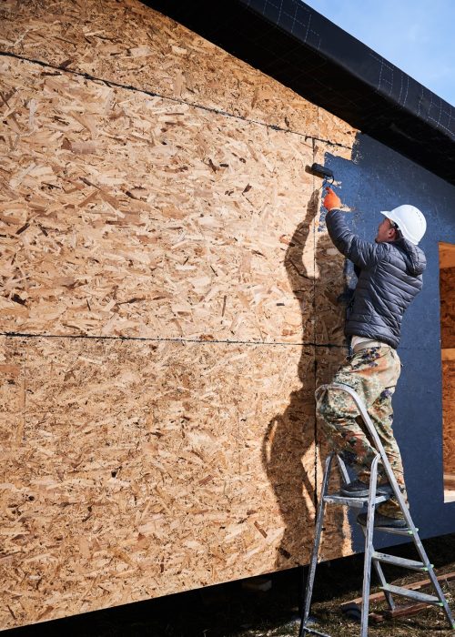 Male painter using paint roller, doing exterior paint work while building wooden frame house.