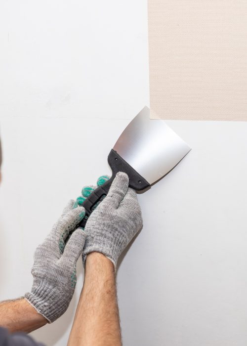 worker hand tear off old light wallpaper with scraper from wall.Repair in the apartment, removing